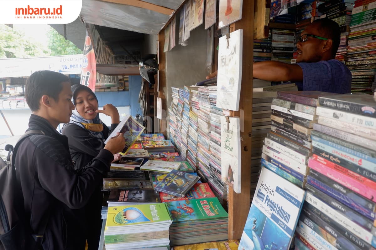 Dua orang pengunjung sedang melihat-lihat buku di lapak buku bekas Stadion Diponegoro Semarang. (Inibaru.id/ Audrian F)