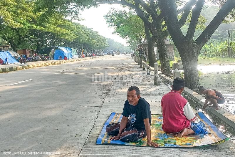 Seorang warga terdampak banjir tetap melaksanakan ibadah salat beralas tikar di Jalan Pantura Demak-Kudus.
